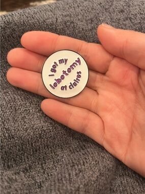 White Enamel Round Pin with Purple Text - "I got my lobotomy at Claire's"